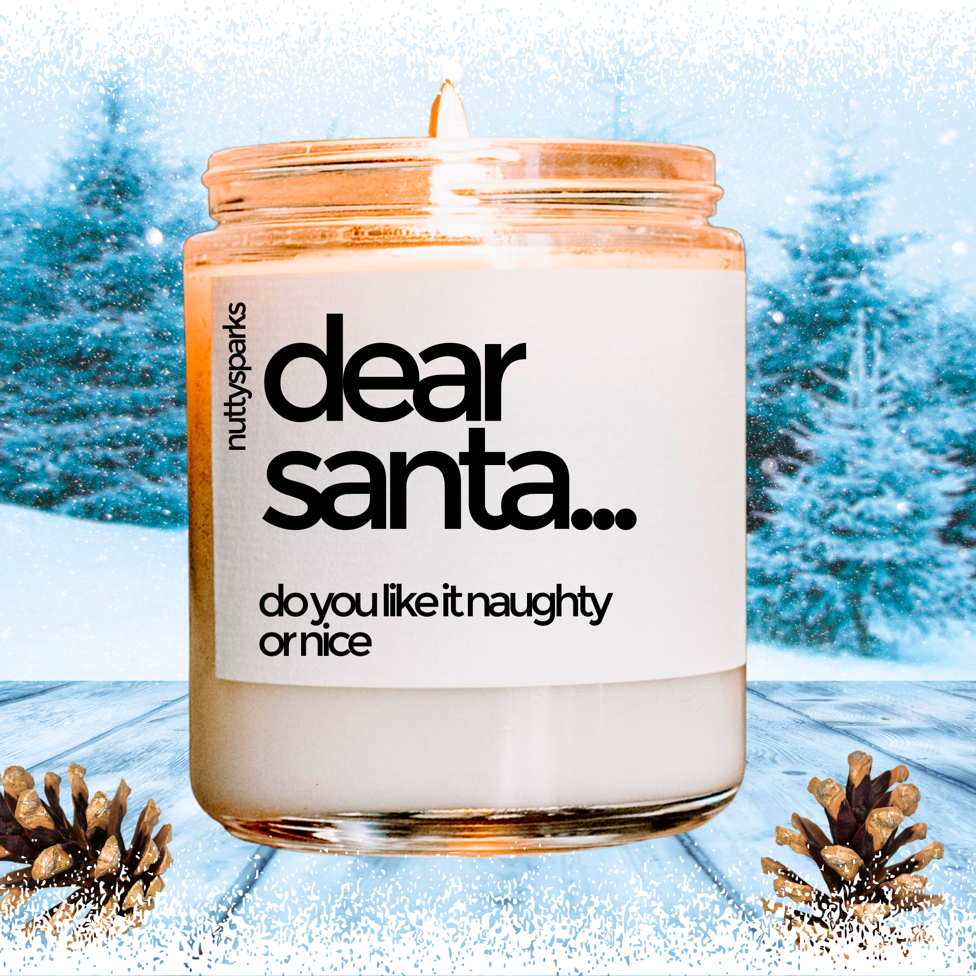 A white candle with a label that says "Dear Santa... do you like it naughty or nice" is placed on a snowy surface with pine cones in the background.